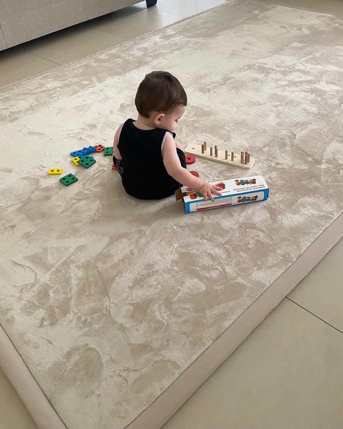 Toddler playing with a shape-sorting toy on a large beige Misk Mat 35mm memory foam mat in a bright living room.