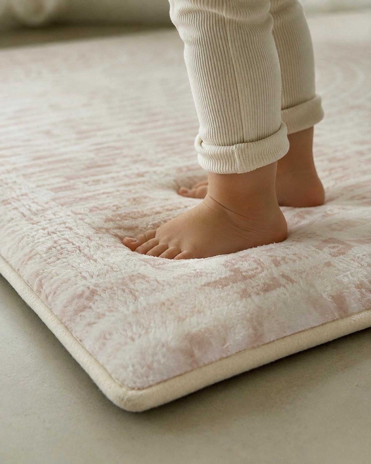 Close-up of a toddler's feet standing on a blush patterned Misk Mat 35mm memory foam mat.