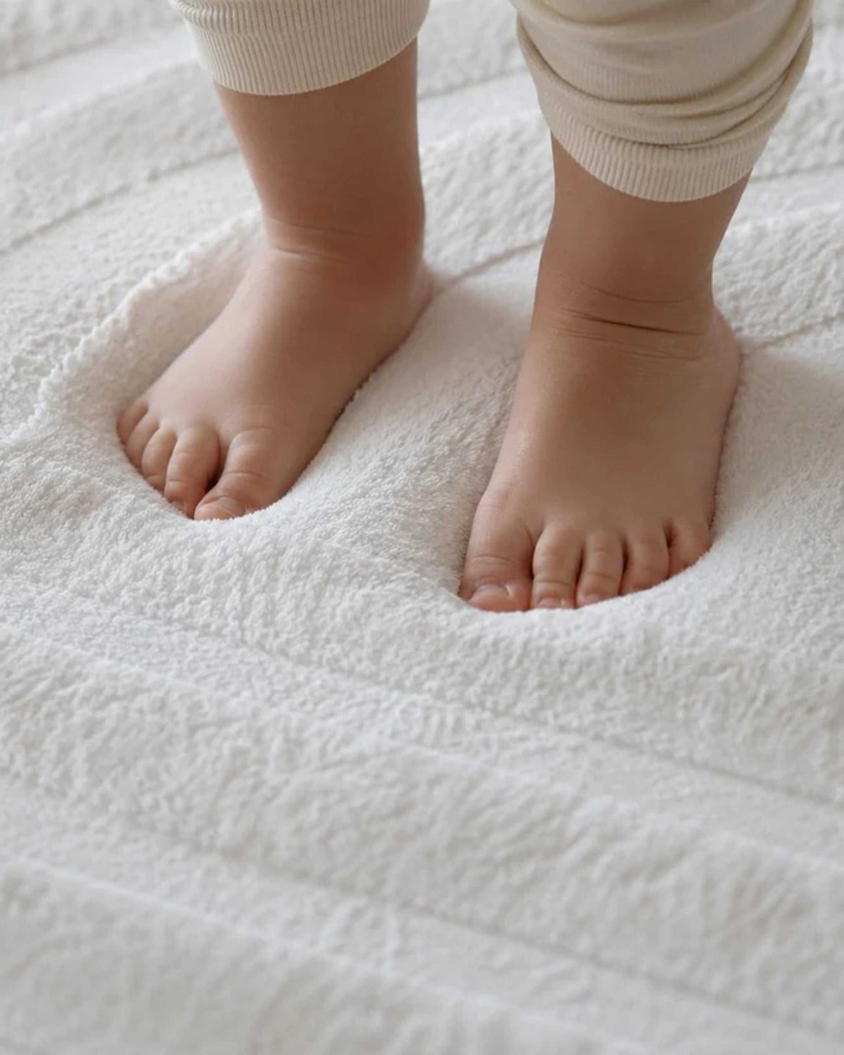Close-up of a toddler's bare feet standing on the soft, textured surface of a Vanilla Cream Misk Mat memory foam mat.
