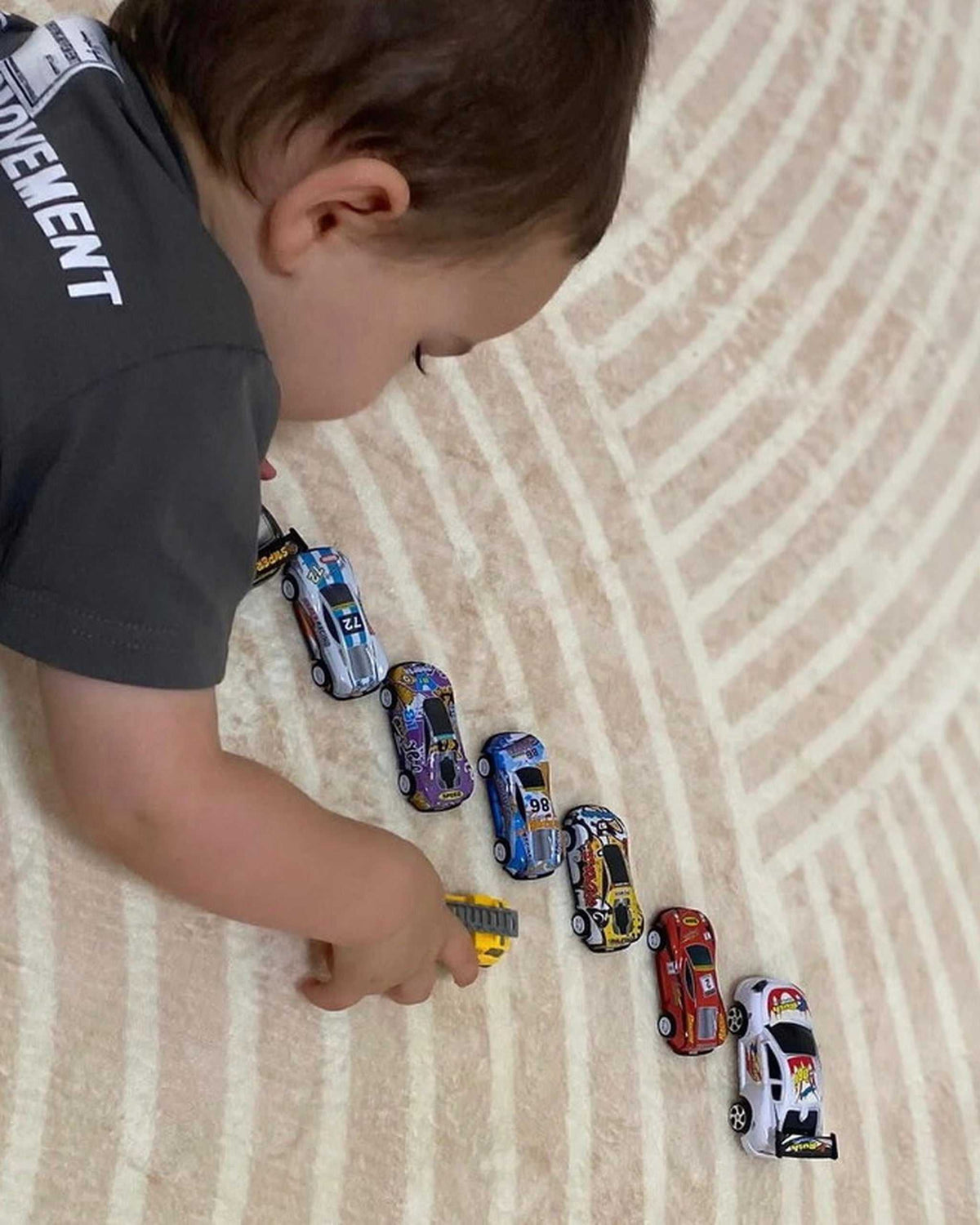 Toddler lining up toy cars on the textured surface of a cream Misk Mat 35mm memory foam mat.