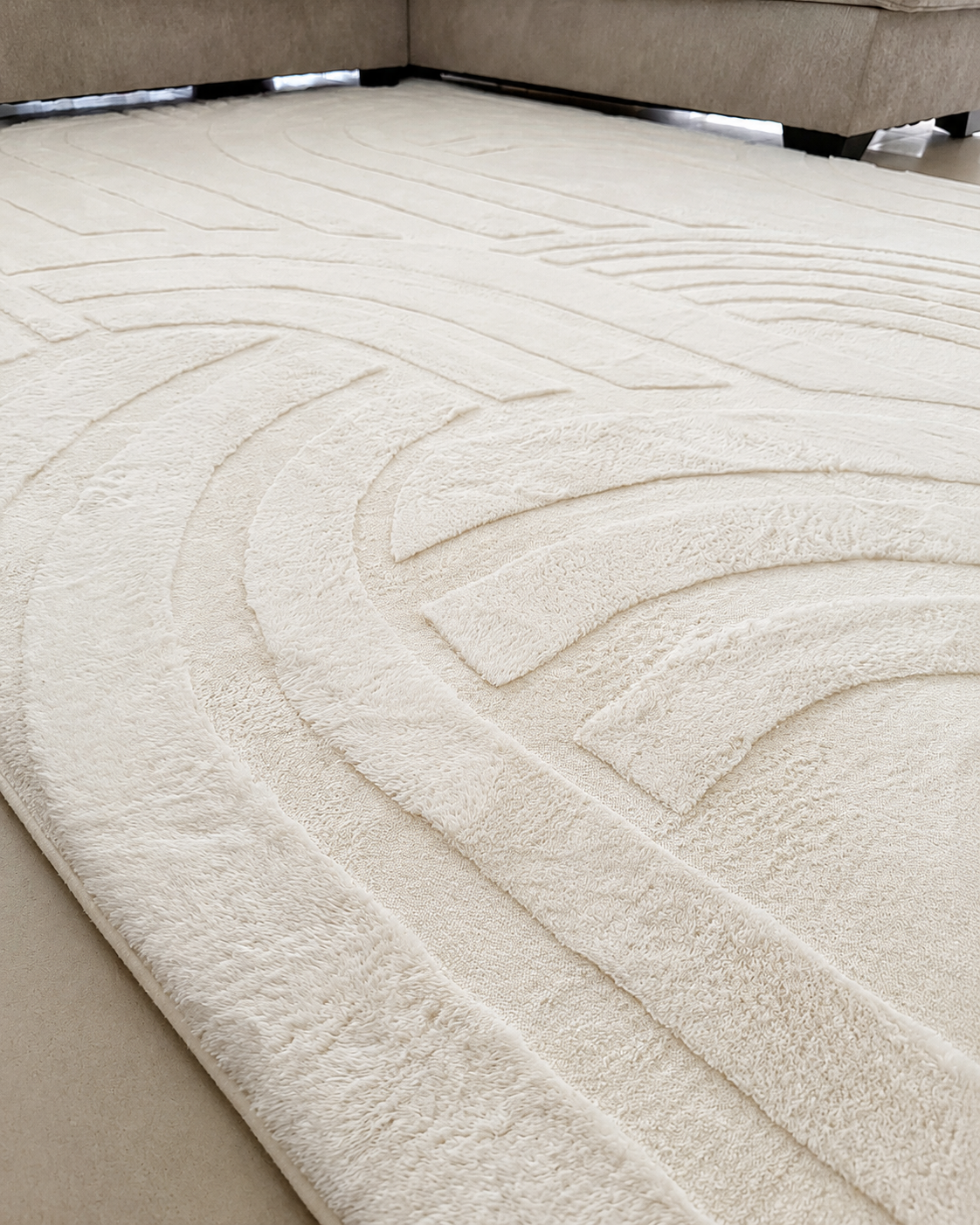 Close-up of the Vanilla Cream Misk Mat's raised 3D arch-pattern texture, with the mat's rounded edge on a wood floor.